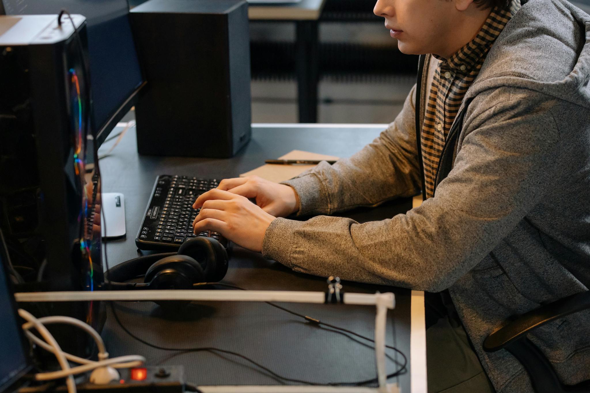Focused young adult typing on keyboard at modern workspace with headphones nearby.