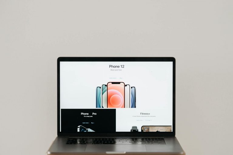 Laptop on stool showing sleek iPhone 12 ad, white background.
